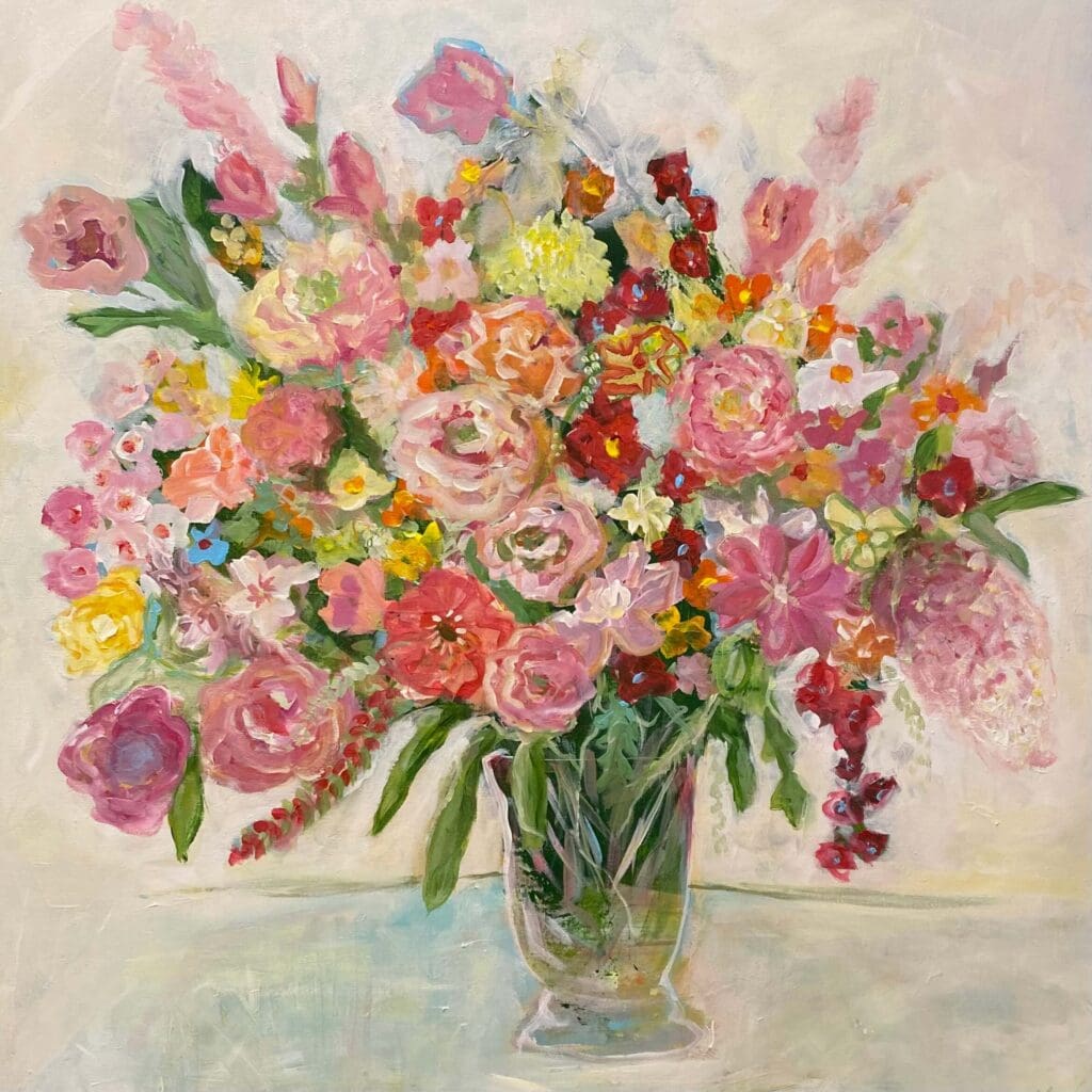Et fargerikt blomsstermotiv av en blomsterbukett i vannglass stående midt på et bord, der blomster i varme rosafarger og gultoner velter utover, med en lys beige bakgrunn som får blomstene til å poppe ut av lerreter